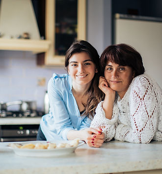 Two women standing together in a kitchen with a snack platter nearby, smiling and enjoying time together