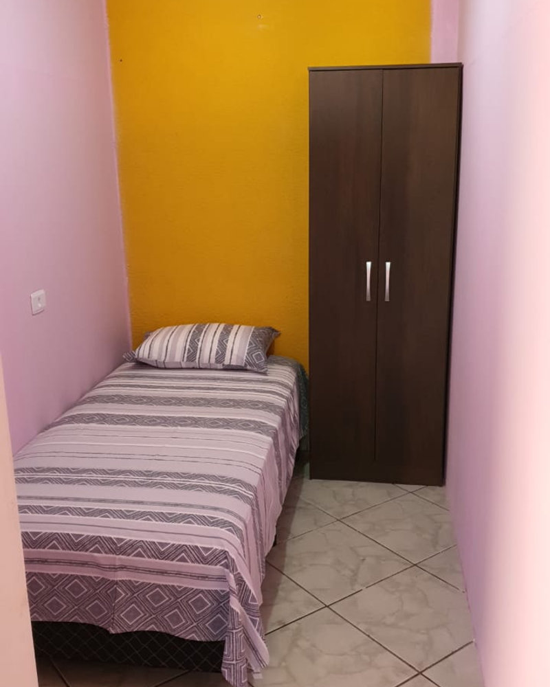 Quarto mobiliado com parede amarela e cama de solteiro
