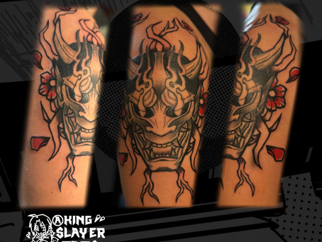 Bold black Japanese graffiti-style Oni mask tattoo with stipple shading, accented by colored sakura petals and branches for striking contrast and modern-traditional fusion.