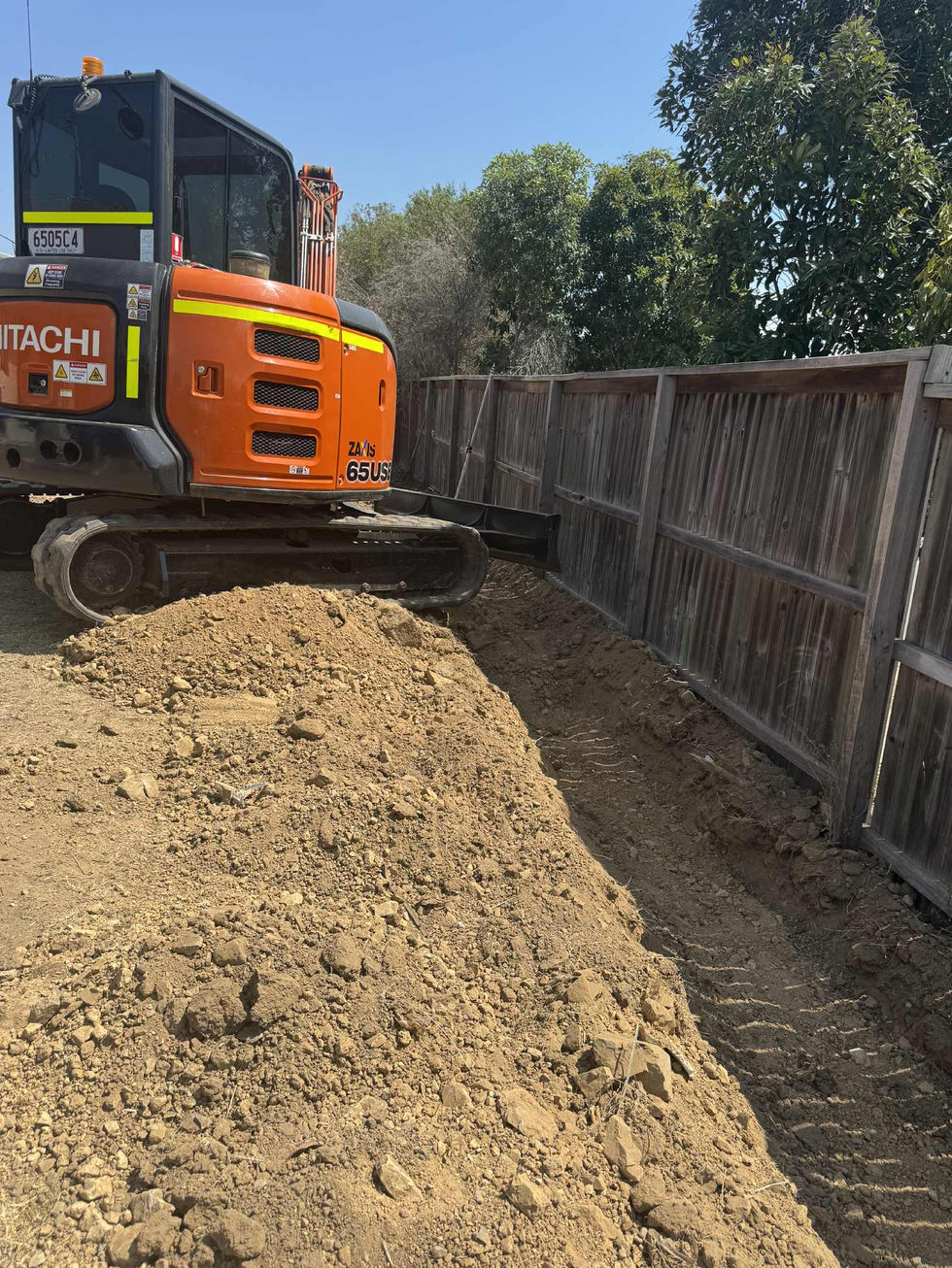 Hitachi excavator digging a trench next to a fence