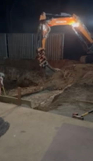 Excavator performing a pool dig at night under work lights