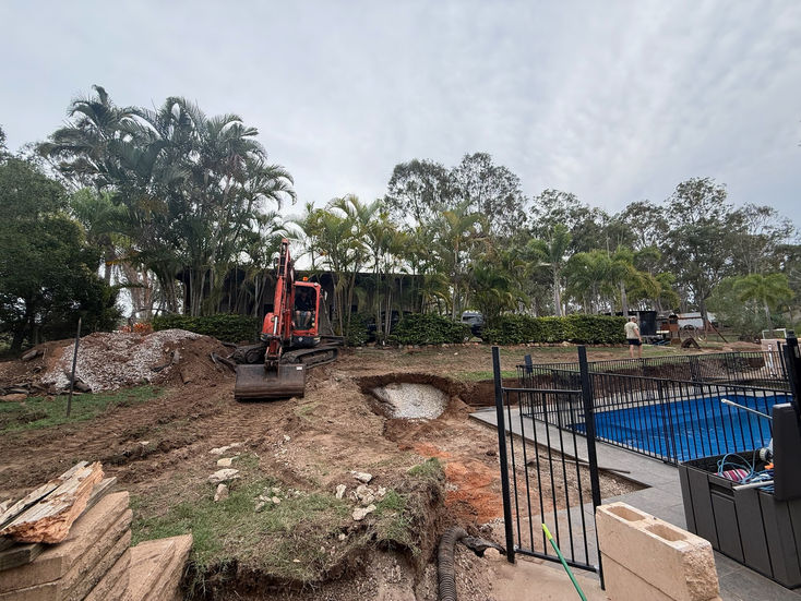 Excavator digging earth next to a pool for a retaining wall.