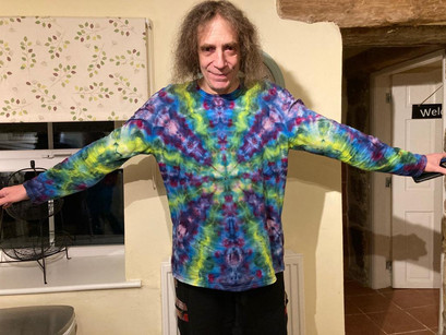 Ed Wynne from Ozric Tentacles, smiling and posing to show off his twisty tie dyed long sleeve t-shirt.