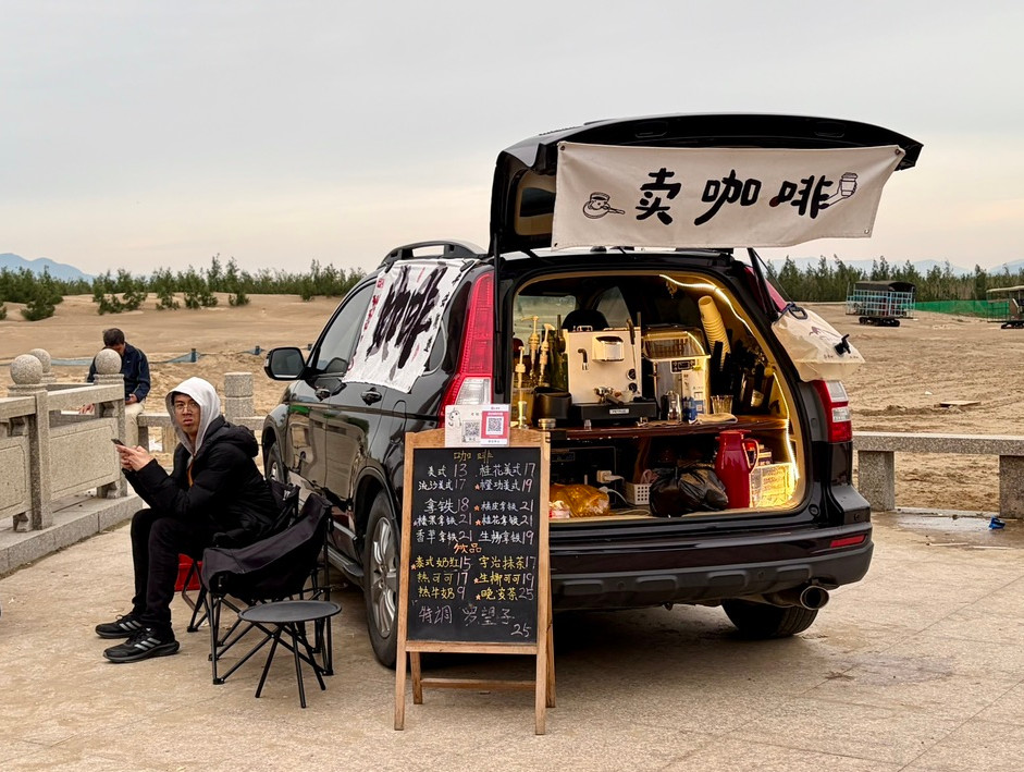 May, 2026. Fuzhou, China. A young man at local seaside cultural market, reflects the flexible employment in China: one car, one espresso machine, one hand-written menu. Image: Claire Dong