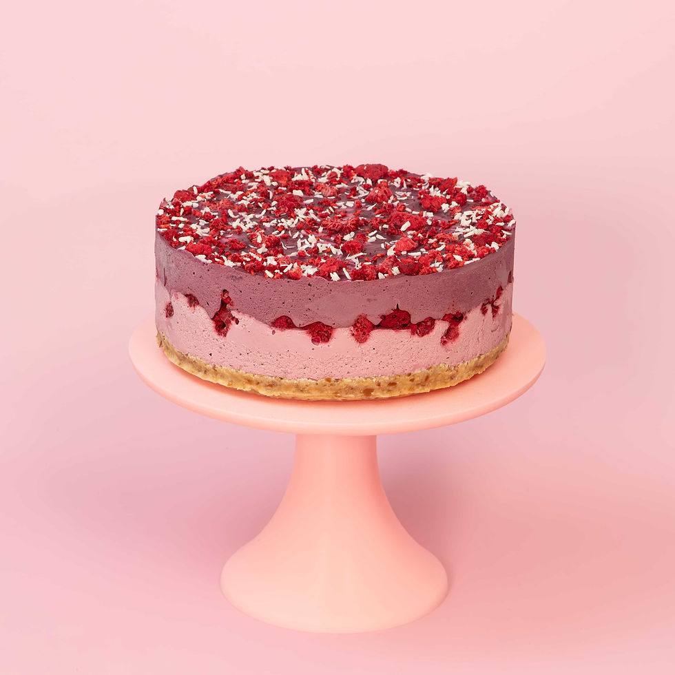Eine vegane glutenfreie Himbeer-Heidelbeer-Torte auf einem rosa Cake Stand vor rosa Hintergrund.