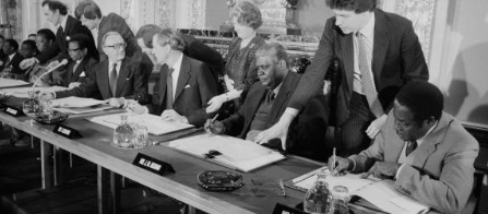 Black-and-white photograph of Zimbabwean nationalist leaders and British officials seated at a long table signing the Lancaster House Agreement in London in 1979, the treaty that ended white-minority rule in Rhodesia and established Zimbabwe as an independent nation.