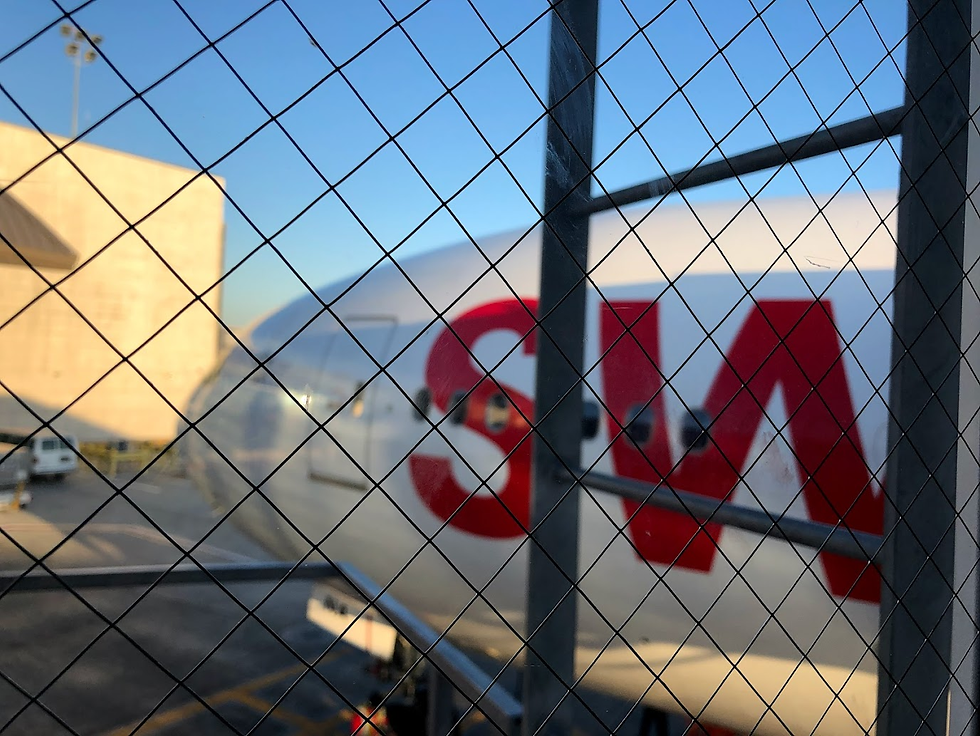A Swiss Air airplane seen through a wire mesh fence at an airport gate, partially obscured by a metal pole, with only the red letters “SW” visible on the aircraft's body.