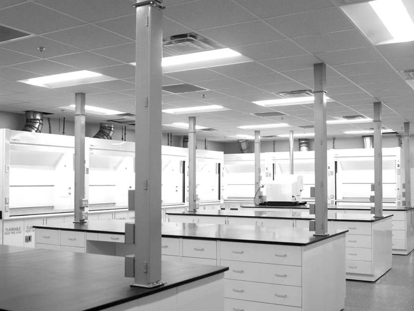 NYCO America laboratory interior in Newnan, GA, featuring fume hoods, black countertops, white cabinetry, and overhead utility connections (black & white).