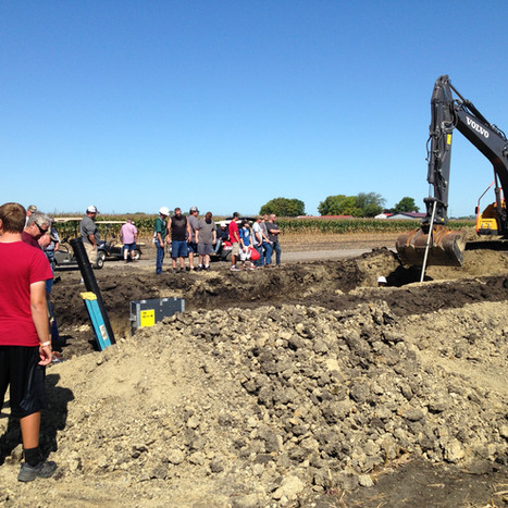 A group of people watching an excavator dig a pit