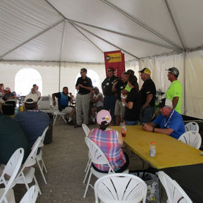 Group of people at tables under a large white tent.