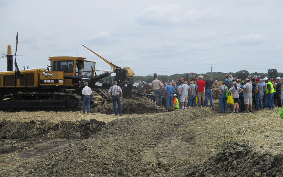 Group of people in a field near a tile plow