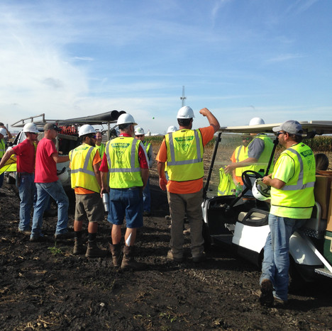 Men in yellow vests standing next to a golf cart in a field