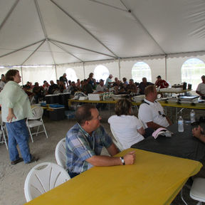 Group of people at tables under a large white tent.