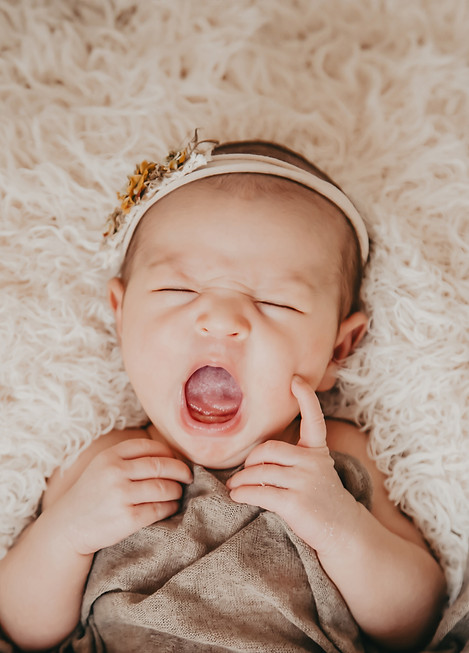 Yawning newborn in a book photography session on a rug.