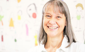 Frau lächelt vor Kinderzeichnung, Beate Kurz, sie steht fröhlich lächelnd im Raum.