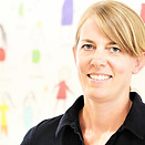 Porträt einer lächelnden Frau; Hintergrund mit Kinderzeichnungen an der Wand.