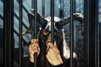 Figure in horned mask gripping bars for adult playroom discipline photography