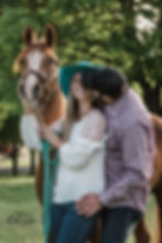 Man kissing cowgirl while she is holding her horse.