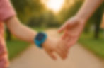 Main d’un parent et d’un enfant se lâchant doucement, montre GPS visible, lumière douce de fin de journée