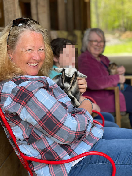 Image is of the owner holding a baby goat and her family in the background