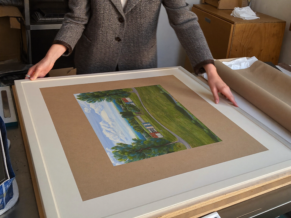 A person steadies a large matted landscape print on a protective backing board.