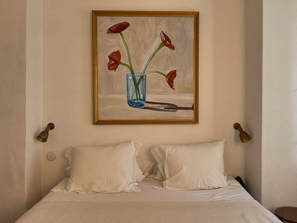 Floral painting hanging above an upholstered bed in a sunlit bedroom