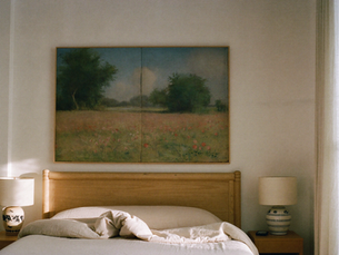 Large vintage misty meadow wall art above a cream linen bed in a calm neutral bedroom.