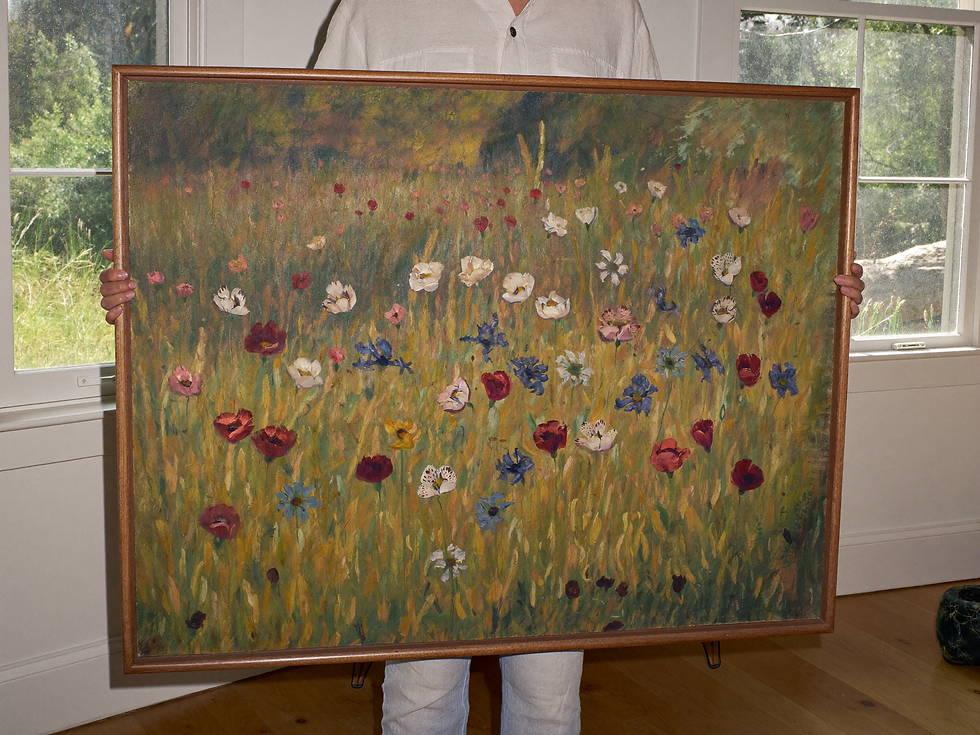 Collector holding a large framed wildflower meadow painting beside a sunlit window.