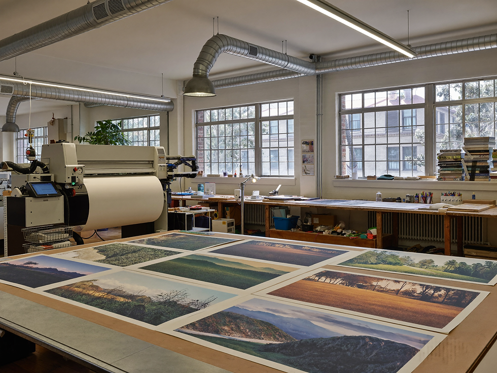 Large printing equipment and landscape proofs in a bright professional studio.