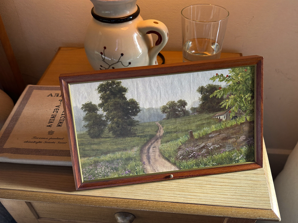 Small framed countryside landscape print styled on an oak bedside table in soft afternoon light.