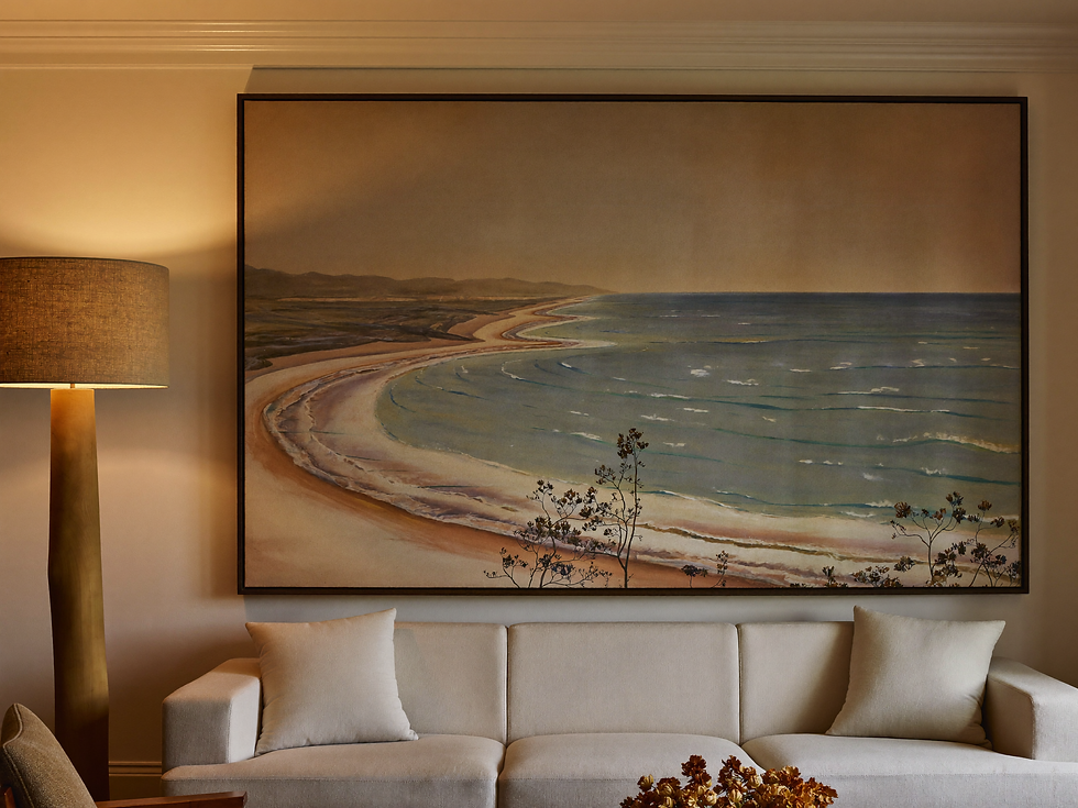 Warm neutral living room at dusk with softly lit vintage coastal landscape art as the visual center.