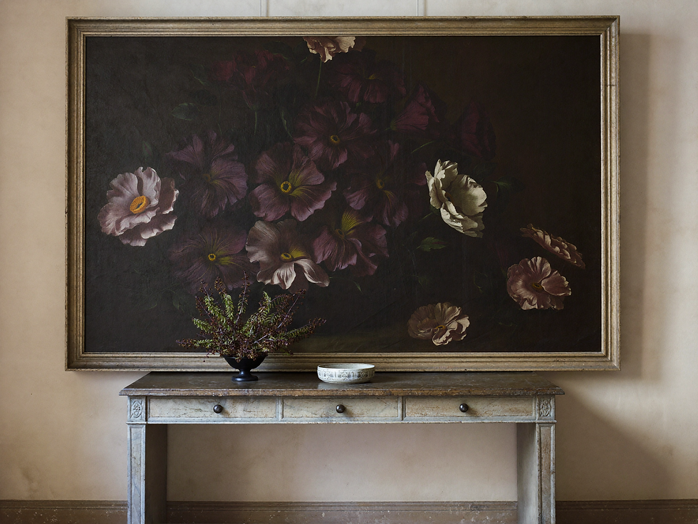 Timeless floral still-life painting above a narrow antique console on a plaster wall.