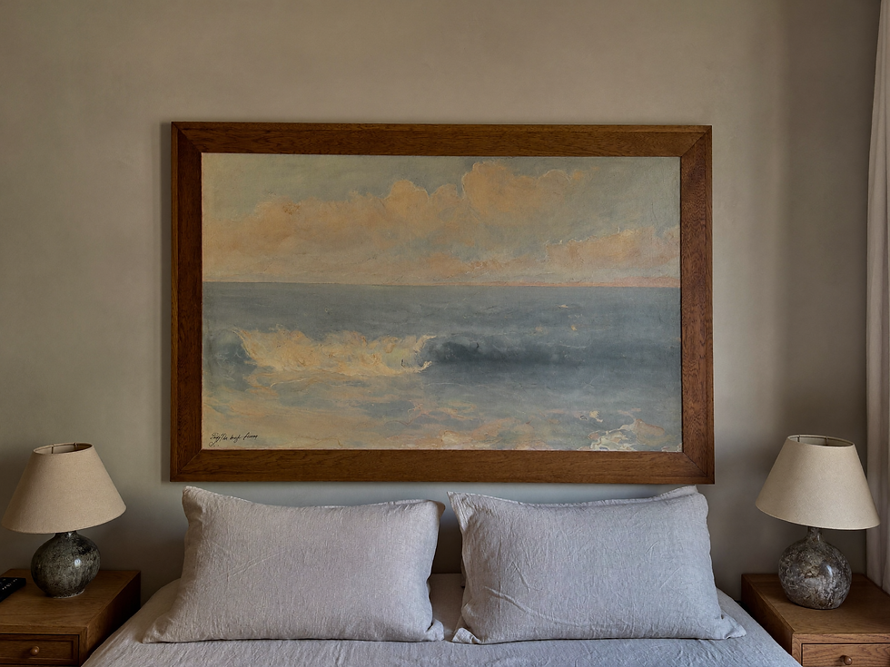 Large vintage seascape painting above an oak bedside table in a calm bedroom.