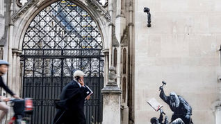  A judge in a wig walks in front of a Banksy painting.