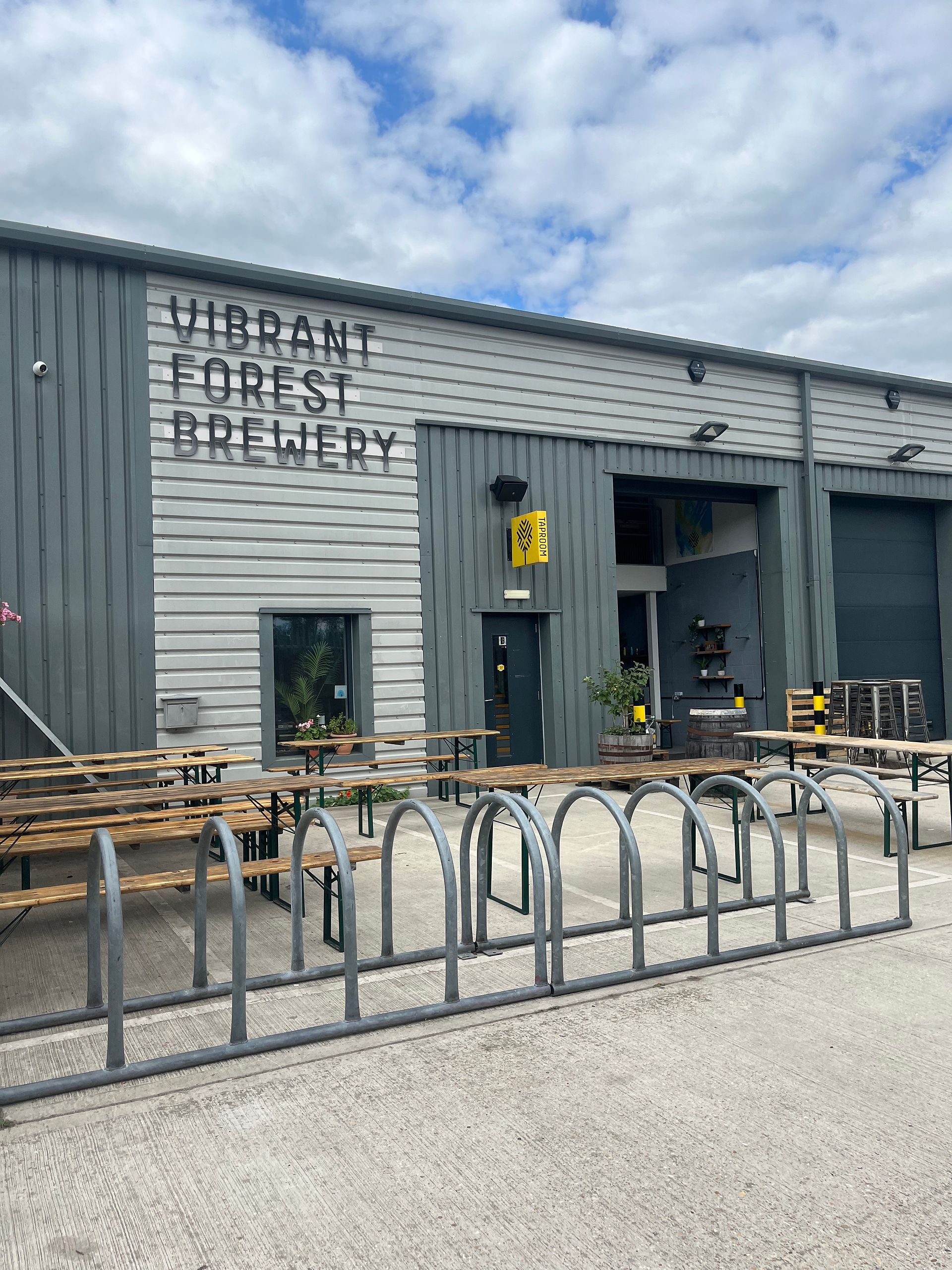 A modern Brewery building, with bike racks and picnic tables outside.