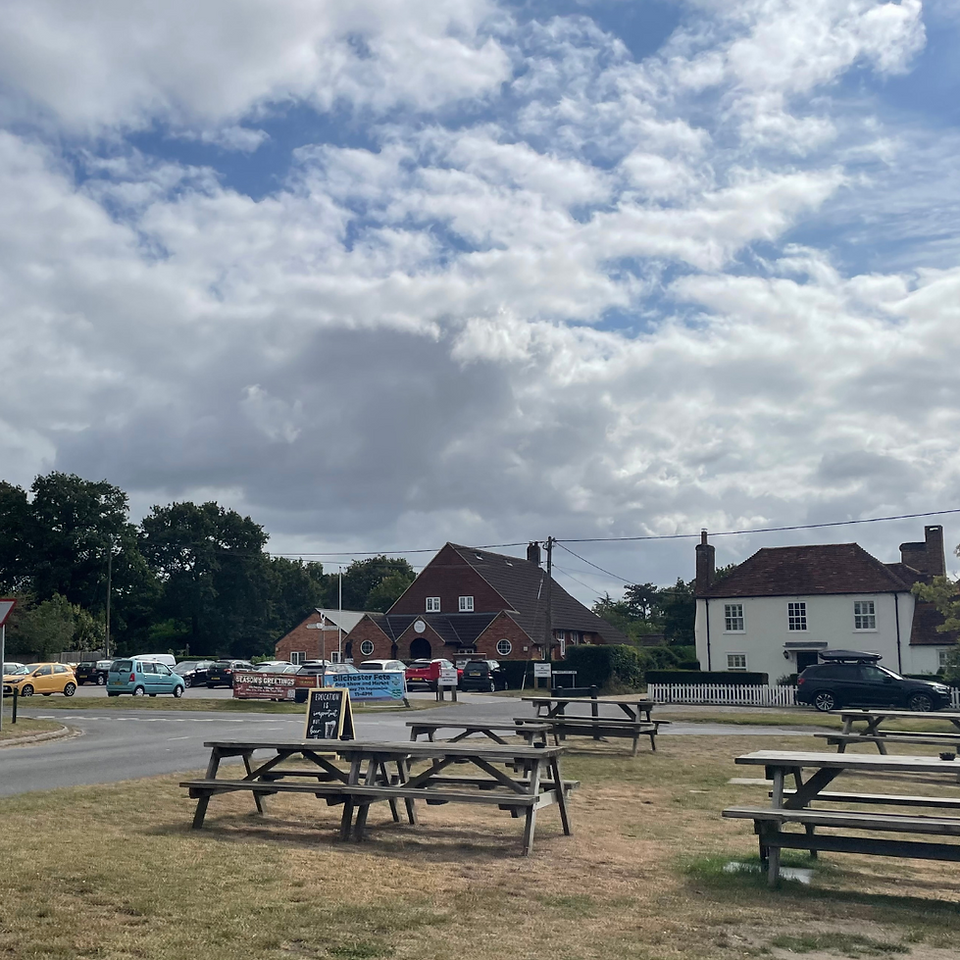 Picnic benches are laid out on a large grass area, in the distance is a pub