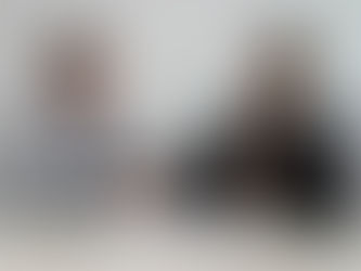 Two men in suits shake hands across a table with documents. A friendly, professional setting with a simple white background.