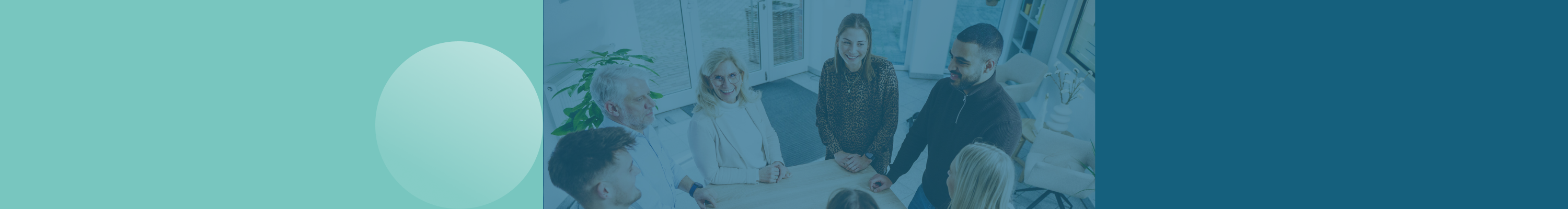 6 Mitarbeiter*innen stehen an einem Tisch im Flur zusammen und lächeln sich gegenseitig an