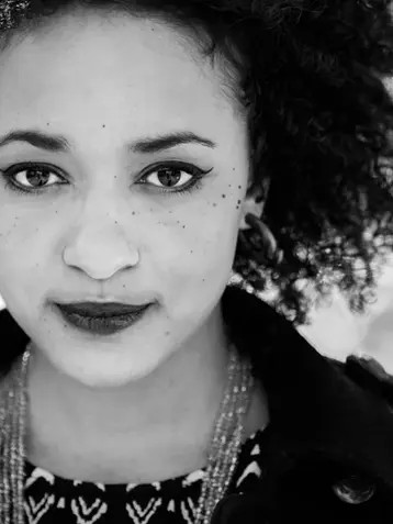 Portrait en noir et blanc d’une femme africaine, Joanne Tatham au regard intense, photographiée en lumière naturelle avec un arrière-plan urbain flou, par Frédéric Pace.