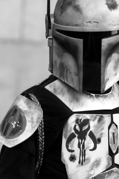 Cosplay d’un mercenaire mandalorien en armure complète, avec casque iconique et plastron décoré du symbole mythosaure. Référence visuelle forte à l’univers de Star Wars, notamment les personnages de Boba Fett et Jango Fett. L’image en noir et blanc accentue l’aspect brut et légendaire du guerrier.