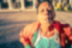 A woman in Havana leans towards the camera with a cigar in her mouth, smiling confidently in bright afternoon sunlight with colourful three-wheeled taxis in the background