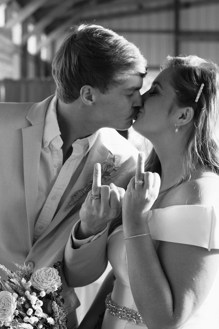 bride and groom kissing holding their ring fingers up