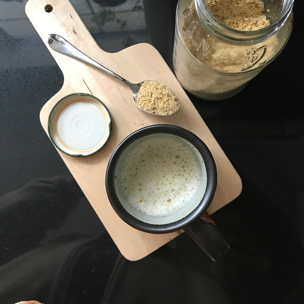 Cup of Masala Milk on wood chopping board with spoonful of masala powder.