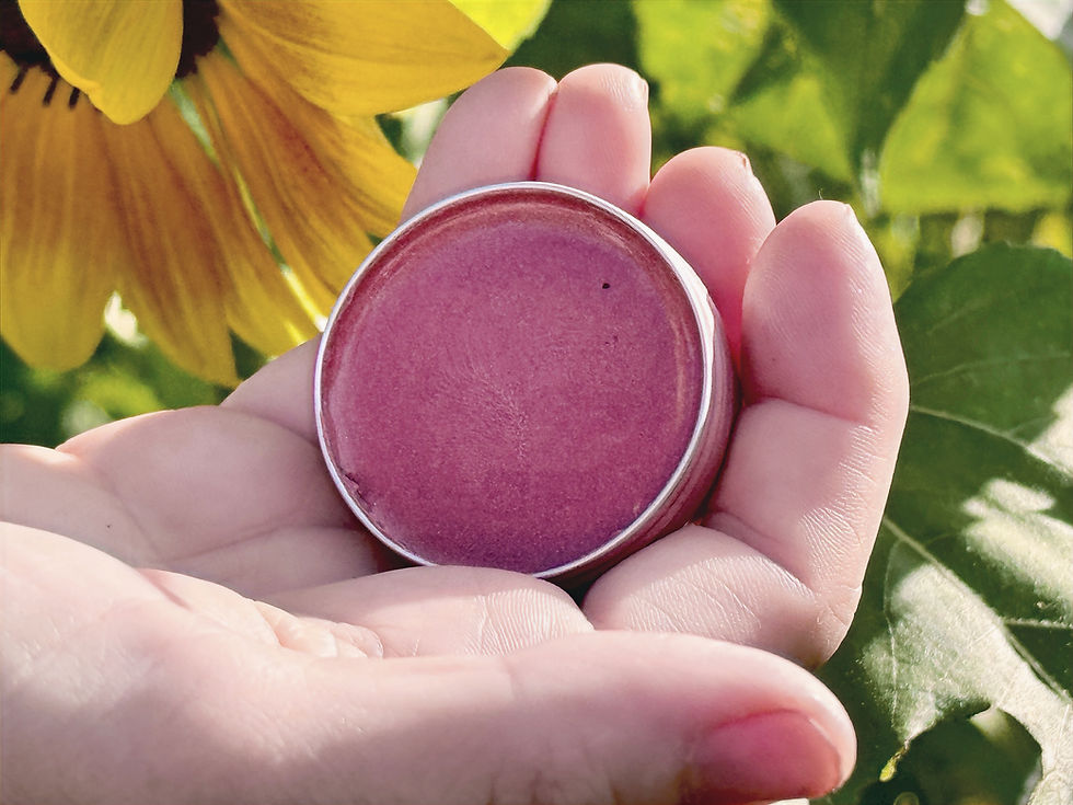 A woman holding a gold pink lip and cheek balm with a sunflower in the background