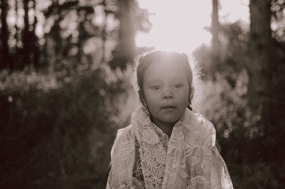 Little girl looking out while wrapped in a lace cloth with the sun setting behind her for a summer f