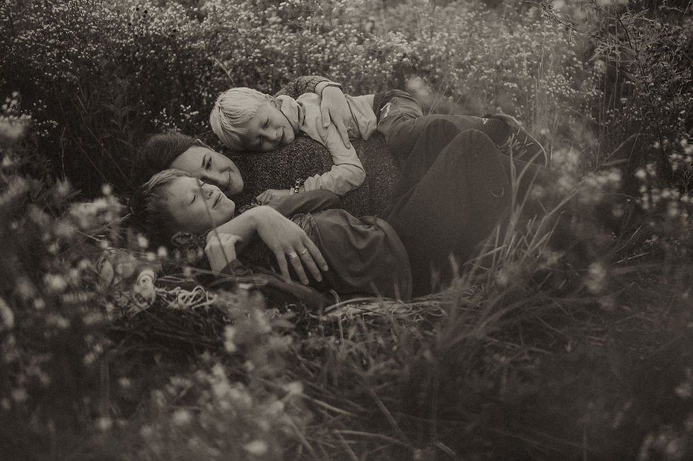 Mother holding her sons in a bed of flowers for a fall family photo session.