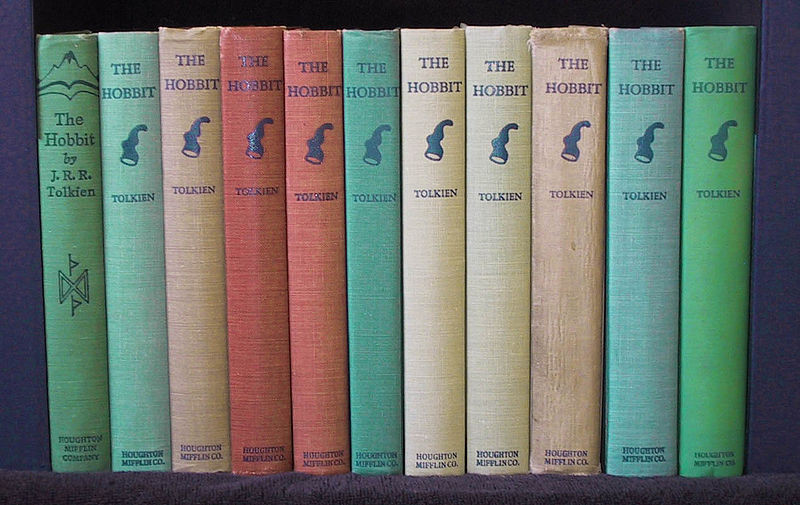 A line of old editions of The Hobbit are lined up on a bookshelf.