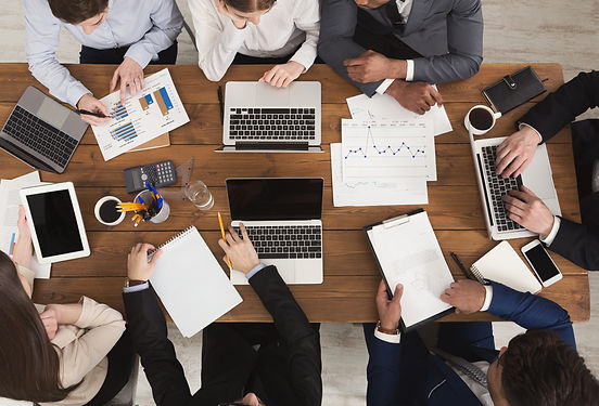 Businesspeople sit round a table and look at graphs and files and have their laptops open