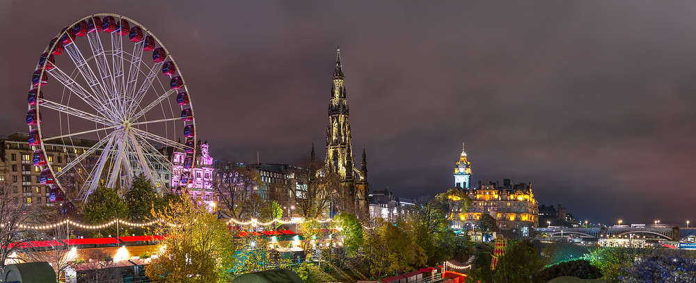 A photo taken at night of a festival in a city featuring a Ferris wheel, lights and tents.