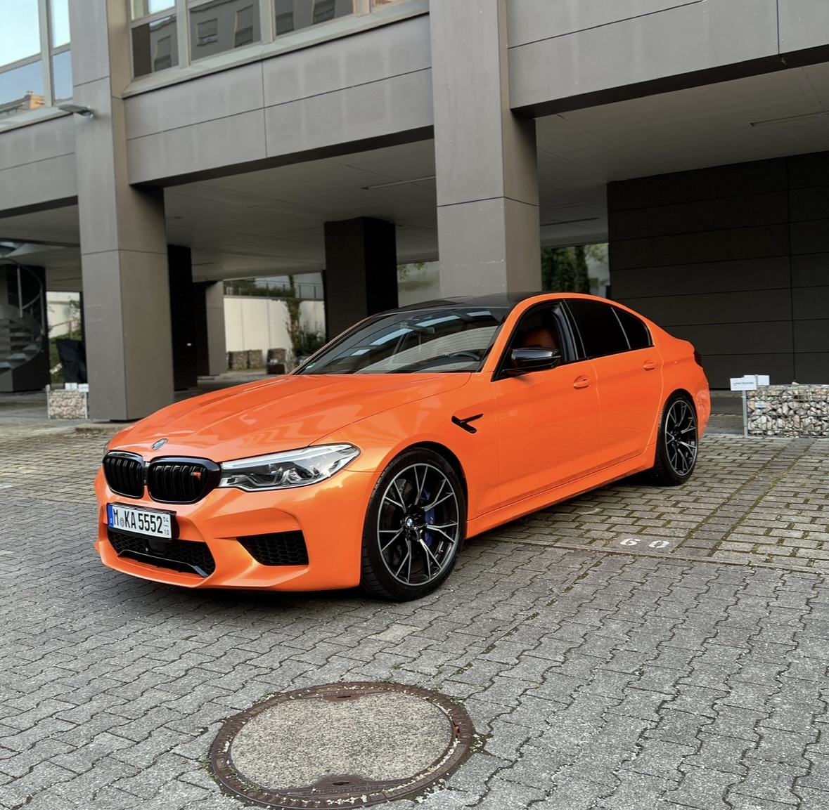 Leuchtend oranger BMW vor Gebäude, Tageslicht, fast quadratisch